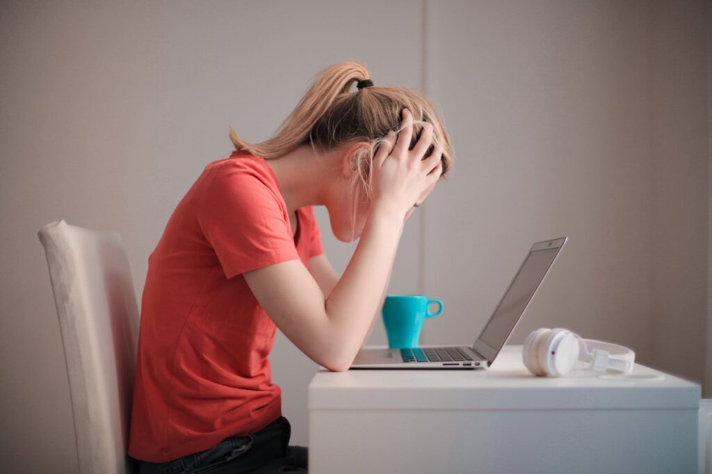 woman in red t shirt looking at her laptop suffering stress and burnout